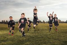 a group of young children playing soccer on a field with their hands in the air