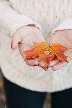 a woman holding out her hands with a leaf in it's palm while wearing a white sweater