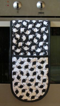 a oven mitt with black and white coffee cups on it, hanging from an oven door