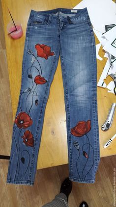 jeans with red flowers painted on them sitting on a wooden table next to scissors and other items