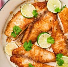 fish with limes and cilantro on a white plate next to a pink napkin