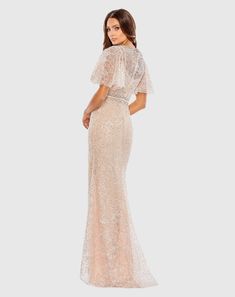 a woman in a nude colored gown with sheer sleeves and an open back, looking at the