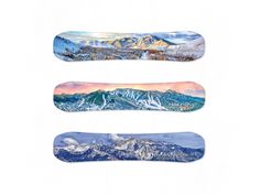 three snowboards with mountains in the background and blue skies above them on a white surface