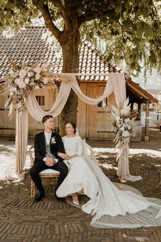 a bride and groom sitting on a bench under a tree