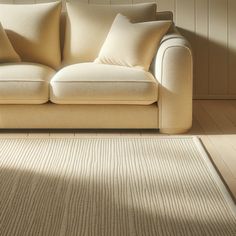 a beige couch sitting on top of a wooden floor next to a white rug in front of a wall