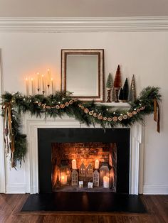 a fireplace decorated with candles and greenery next to a mirror on top of the mantle