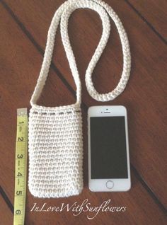 a cell phone is laying next to a crocheted purse and measuring tape on a wooden table