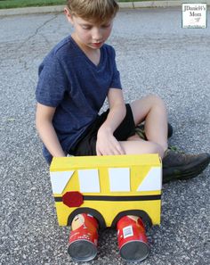 a young boy sitting on the ground next to a cardboard school bus