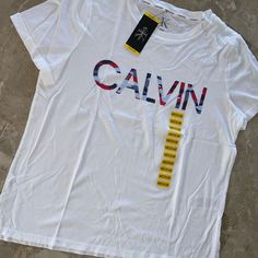 Calvin Klein Women's Graphic Tee Shirt Rolled Sleeve Graphic Logo At Chest Soft Crew Neck Cotton Blend 60 % Cotton 40% Model Calvin Klein White Logo Print T-shirt, Calvin Klein White Short Sleeve Top, Calvin Klein White Tops With Logo Print, Calvin Klein Relaxed Fit Letter Print Top, White Calvin Klein Crew Neck T-shirt, Calvin Klein Summer T-shirt With Logo Print, Calvin Klein White Crew Neck T-shirt, Calvin Klein Graphic Print T-shirt For Summer, Calvin Klein Logo Print T-shirt For Summer