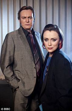 a man and woman standing next to each other in front of a wall with vertical blinds