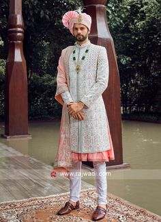 a man standing on top of a rug wearing a white suit and pink turban