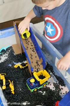 a young boy playing with toys in a plastic container filled with black gravel and sand