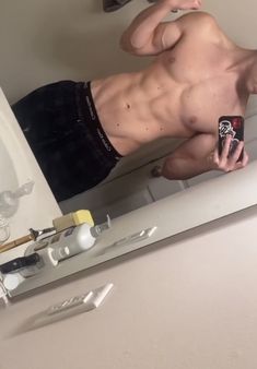 a shirtless man taking a selfie in front of a mirror with his cell phone