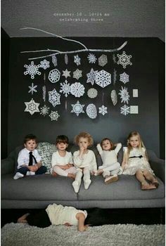 four children sitting on a couch in front of a black wall with snowflakes hanging from it