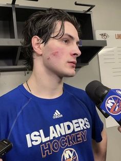 a man in a blue shirt is holding a microphone and talking to the camera while wearing a t - shirt that says islanders hockey