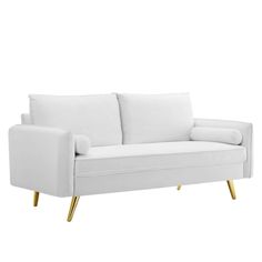 a white couch sitting on top of a wooden floor next to a white wall with gold legs