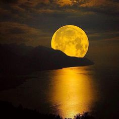 the full moon shines brightly in the night sky over water with mountains behind it