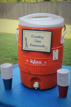 an orange cooler sitting on top of a blue table next to stacks of paper plates