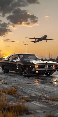 an old muscle car is parked in front of an airplane on the tarmac at sunset