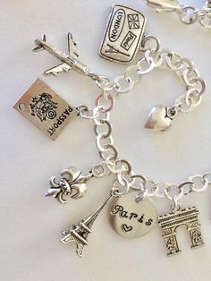 "Adorable Paris charm bracelet featuring 13 detailed silver charms of travel to Paris, classic landmarks, artist quarter, food and drink. Hand stamped 1/2\" 18 aluminum disc says \"Paris ❤️\". Memories of a visit abroad living \"la bonne vie\" in the magical city of Paris! Charms include: suitcase, plane, passport, fleur de lis, Eiffel Tower, Arc de Triumph, artist palette, Sacre Coeur church, Vespa scooter, baguette, cheese, wine, and croissant. Charms are antique silver, pewter and silver tone Silver Charms Jewelry Souvenir, Nickel-free Silver Charms Souvenir, Silver Charm Bracelet As Souvenir, Nickel-free Silver Charms For Souvenir, Personalized Bracelet Jewelry Souvenir, Silver Symbolic Jewelry Souvenir, Personalized Bracelet Jewelry As Souvenir, Personalized Bracelet Jewelry For Souvenir, Silver Nickel-free Bracelet Souvenir