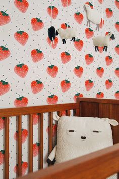 a baby's crib in front of a wall with strawberries and sheep on it