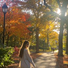 a woman walking down a path in the park with trees and leaves all around her