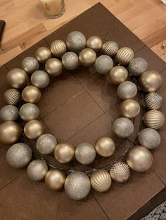 a gold and silver christmas ornament wreath on top of a wooden table with candles