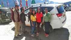 four people standing in front of a van with flags on the back and mountains in the background