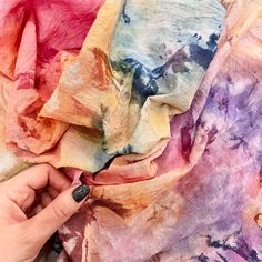 a hand is holding an object in front of a colorful scarf that looks like it has been dyed