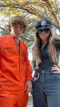 two people in orange jumpsuits standing next to each other and one is holding a pair of scissors