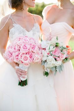 two bridesmaids in white dresses holding bouquets of pink and white flowers together