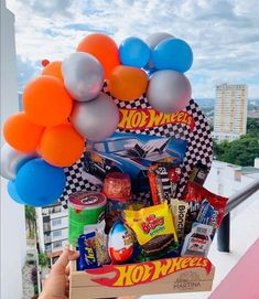 a person holding up a box filled with candy, balloons and candies on top of a roof