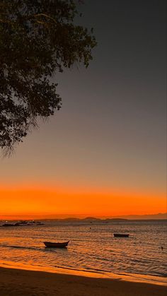 two boats are sitting on the beach at sunset