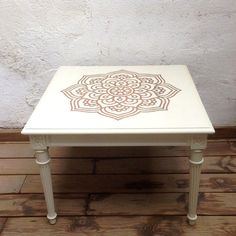 a small white table with an intricate design on the top and bottom, in front of a brick wall