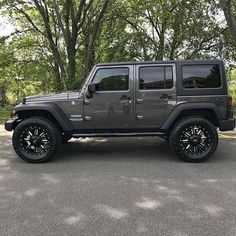 a gray jeep is parked on the side of the road in front of some trees