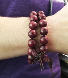 12mm Violet Wood Purpleheart wood beads strung on elastic cord fits a 6.5 inch wrist.  2mm hole. As our mala are hand-carved and assembled from natural materials, bead and tassel appearance may vary.  The beads are 12mm wide.  $12 per bracelet (our model is wearing two bracelets in the photo). Violet Wood Purpleheart meaning: Purpleheart gets its name from the color of the wood.  Its scientific name is Peltogyne.  It has other names in addition to Violet Wood and Purpleheart, such as Amendim and Wooden Beads Rosary Bracelet For Meditation, Meditation Rosary Bracelet With Wooden Beads, Adjustable Wooden Beaded Bracelets With 8mm Beads, Adjustable Wooden Beaded Bracelet With 8mm Beads, Spiritual Wooden Beads Stretch Bracelet For Meditation, Spiritual Stretch Bracelet With Wooden Beads For Meditation, Traditional Wood Bracelets With Round Beads, Traditional Wooden Bracelets With Round Beads, Traditional Wooden Bracelet With Round Beads