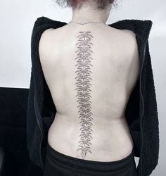 the back of a woman's body with a fern tattoo on her lower back