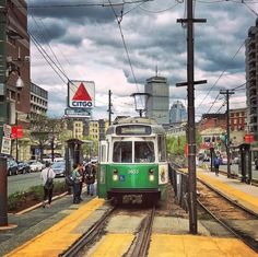 a green and white train traveling down tracks next to tall buildings on a cloudy day