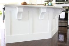 a white kitchen with an island in the middle and wood flooring on the other side