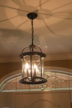 a chandelier hanging from the ceiling with three lights on it and a circular glass window