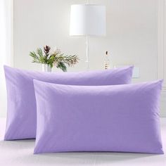 two lavender colored pillows on a bed with a white lamp in the corner behind them