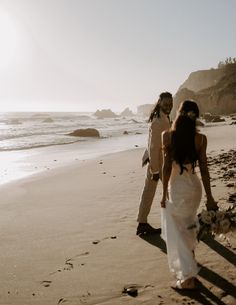 a bride and groom walking on the beach with footprints in the sand near the water