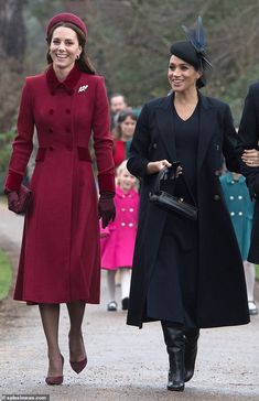 two women in red coats and hats walk down a path with other people behind them