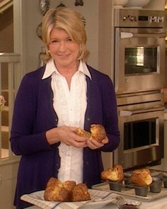 a woman is standing in the kitchen holding some muffins and smiling at the camera