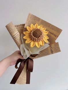 a hand holding a paper sunflower with brown ribbon