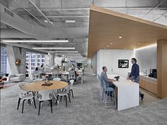 two men are sitting at a table in an office setting with chairs and desks