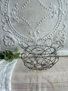 a wire basket sitting on top of a bed next to a white wall with flowers in it