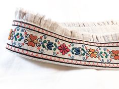 "History of Czech Folk Border: Czech Folk Border features multiple motifs in the Czechoslovakian style.  This original design is inspired from an embroidered child's dress from the 19th century. Originally embroidered on white linen, the design is meant to be a continuous entity on a piece of clothing, curtains, sheets, pillows, or even a belt as shown in the photos! The brown and orange tones contrast with deep green and blue, and will look good with just about anything.   The project I chose to make using Czech Folk Border was a belt! The belt is made from heavy linen; lined in cotton lawn, with a light weight linen upper frayed ruffle. The back incorporates a small section of elastic, a layered flower with button center, and a 1\" long hooked closure hidden under the flower. Please see Bohemian Embroidered Fabric With Border For Spring, Folk Style Cotton Fabric With Embroidered Border, Folk Style Multicolor Embroidered Fabric For Spring, Multicolor Embroidered Folk Fabric For Spring, Cream Bohemian Embroidered Fabric, Bohemian White Embroidered Fabric With Border, White Bohemian Embroidered Fabric, Bohemian White Embroidered Fabric, Folk White Fabric With Embroidered Border