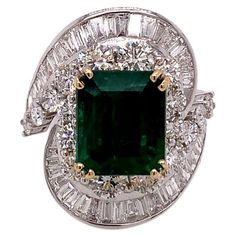 This distinctive ring features a phenomenal 5.39 Carat emerald cut Emerald at its centre, surrounded by a unique arrangement of round brilliant and tapered baguette cut diamonds. The diamonds in this ring weigh a total of 4.03 carats and are set in 18K White Gold, while the Emerald is held in a 18K Yellow Gold claw setting. The rich, green hues of the emerald set in gold and surrounded by sparkling diamonds make this ring a real masterpiece. From our Verde Collection, this ring is Opulence at it Luxury Elegant Channel Set Emerald Ring, Emerald Set, Emerald And Diamond Ring, Emerald Diamond Ring, Claw Setting, Green Hues, Rich Green, Baguette Cut Diamond, Baguette Cut