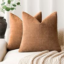 two brown pillows sitting on top of a white couch next to a vase with flowers